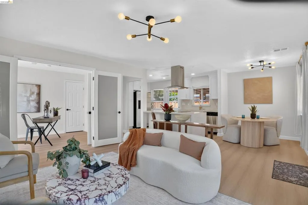 Spacious living area featuring light wood-finish flooring, a contemporary ceiling light fixture, and a built-in kitchen hood