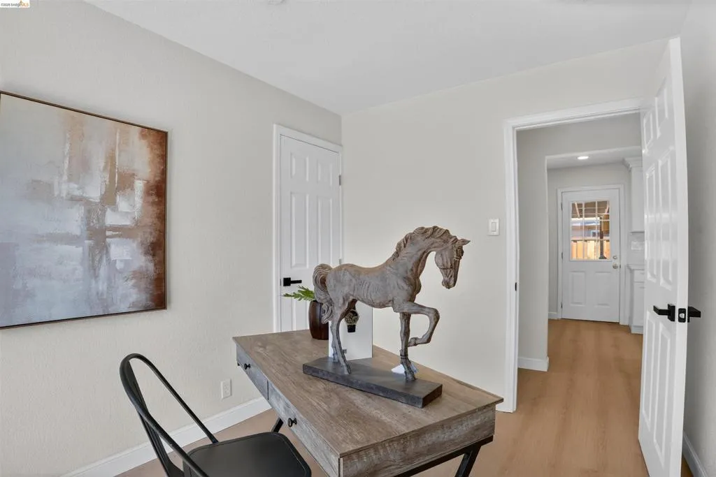 Open doorway revealing wood-finish flooring, white paneled doors with matte black hardware, and light-colored walls