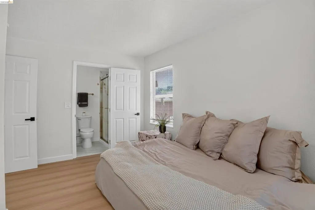 Bedroom featuring light-colored wood-finish flooring, white walls, and a window with horizontal blinds