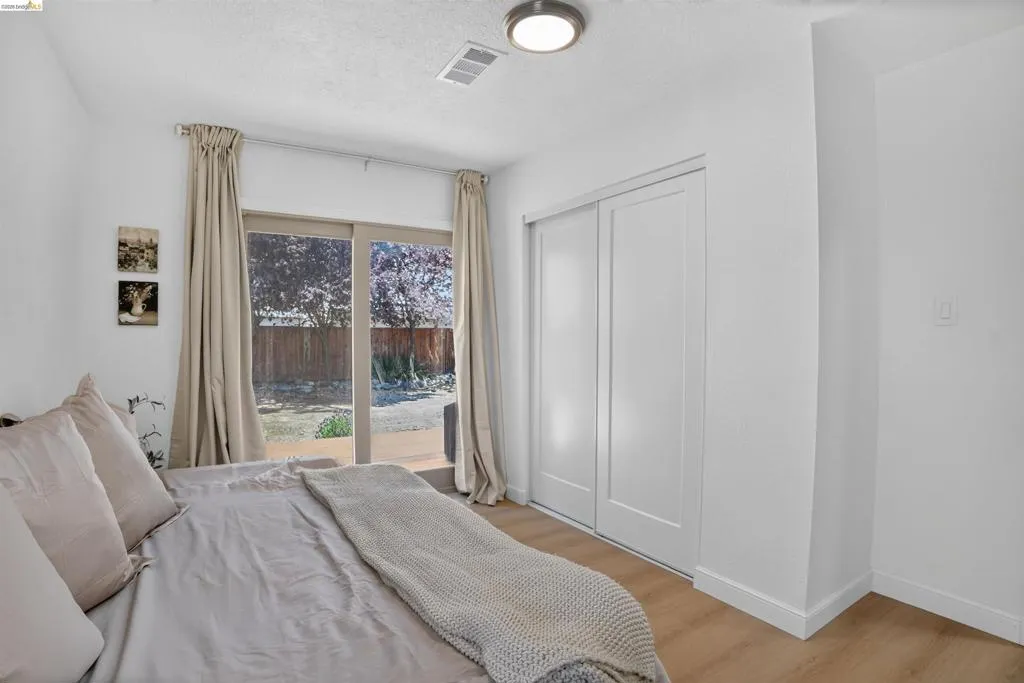 Room featuring sliding glass doors to the exterior, wood-finish flooring, a contemporary ceiling light fixture, and a built-in closet with white bifold doors