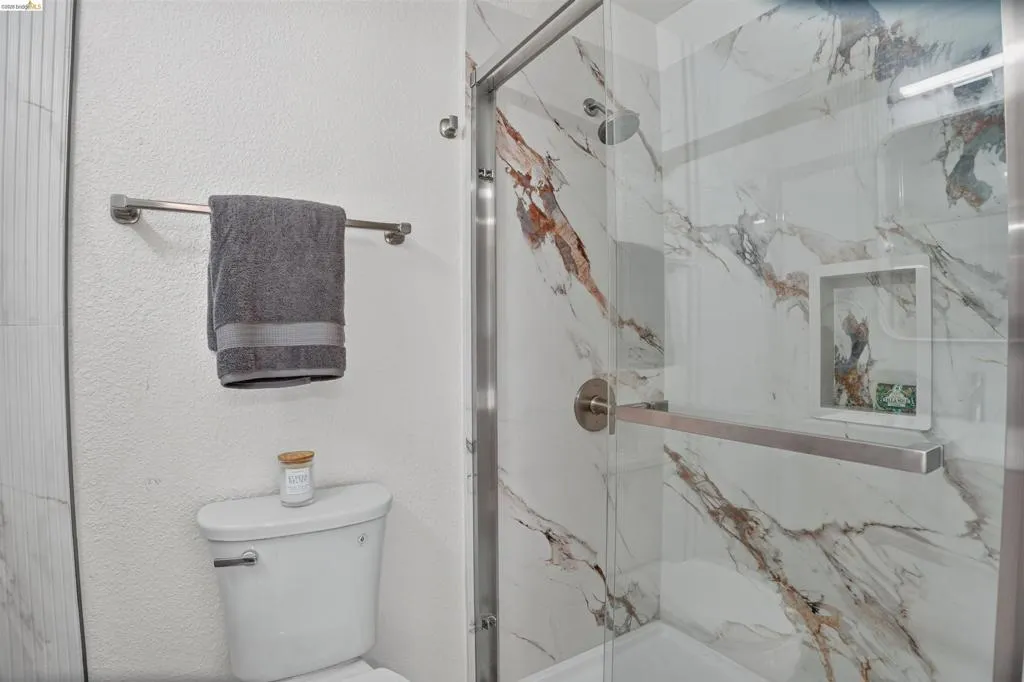 Glass-enclosed shower with a polished chrome frame and a large format tile surround featuring a white base with brown and gray veining