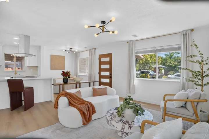 Open-concept living space with wood-finish flooring, a contemporary chandelier, and a modern kitchen featuring a stainless steel range hood and white cabinetry