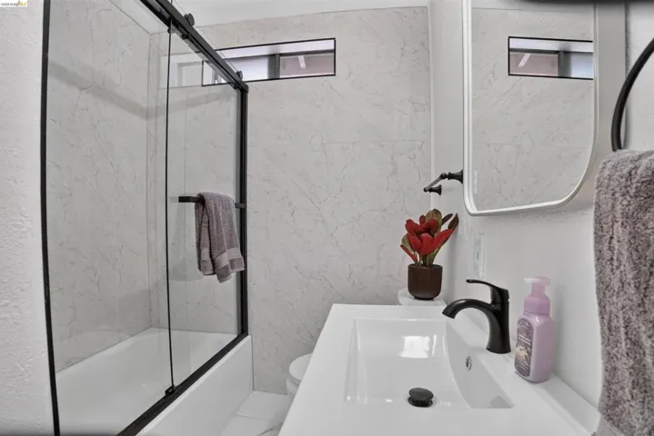 Bathroom featuring a white vanity with an integrated sink, matte black faucet, and a contemporary frameless mirror