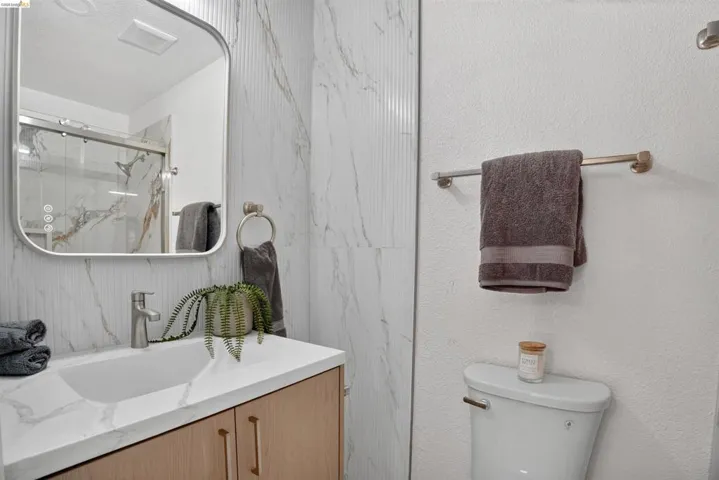 Contemporary bathroom featuring a light wood-finish vanity with a white countertop and integrated sink, brushed nickel faucet, and a wall-mounted mirror