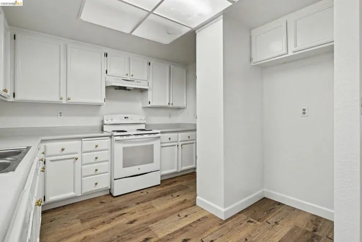 Kitchen featuring extensive white cabinetry with gold-tone hardware, white laminate countertops, and wood-finish flooring