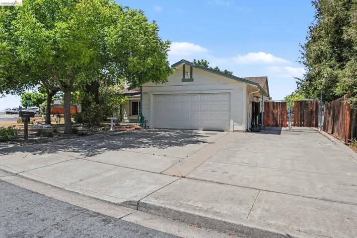 Single-story residence featuring a two-car garage, mature front yard trees, concrete driveway, and a gated side yard access