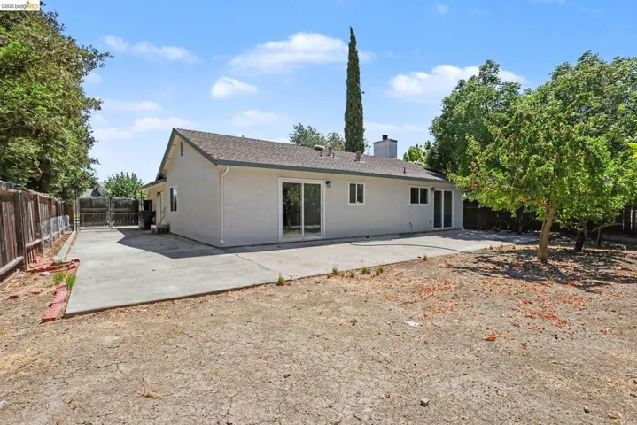 Rear exterior of the property featuring a light-colored stucco finish, a dark shingle roof, and multiple sliding glass doors