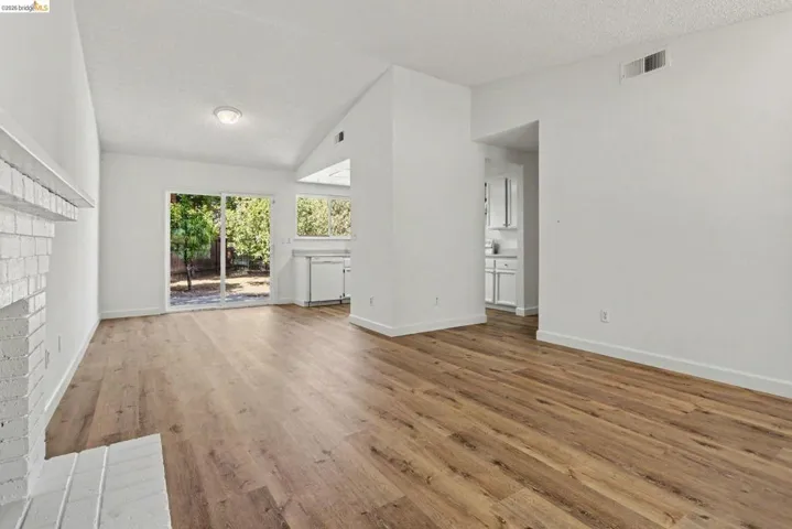 Living area featuring wood-finish flooring, a painted brick fireplace, vaulted ceilings, and a sliding glass door to the exterior
