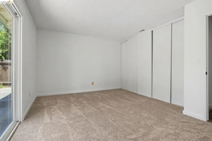 Spacious room featuring neutral carpeting, white walls, multiple sliding closet doors, and a sliding glass door providing exterior access