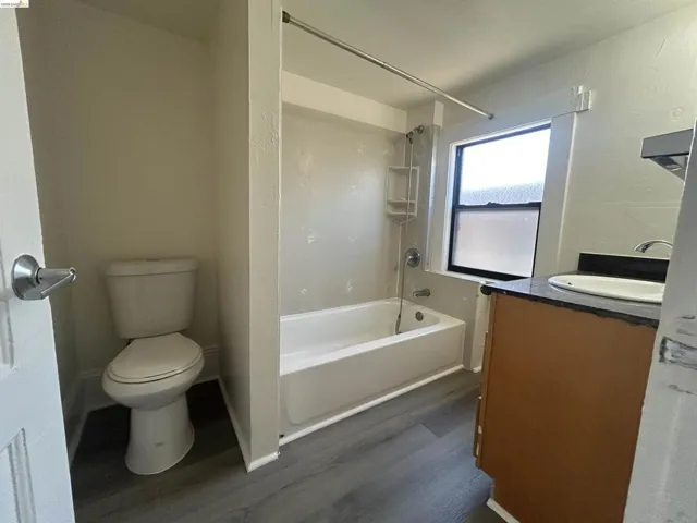 Bathroom featuring a white bathtub, shower with built-in shelving, wood-finish flooring, and a vanity with a dark countertop and undermount sink
