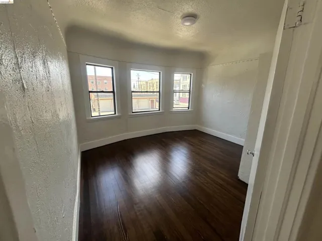 Room featuring dark wood-finish flooring, three windows with white trim, a smooth ceiling with a flush-mount light fixture, and textured walls