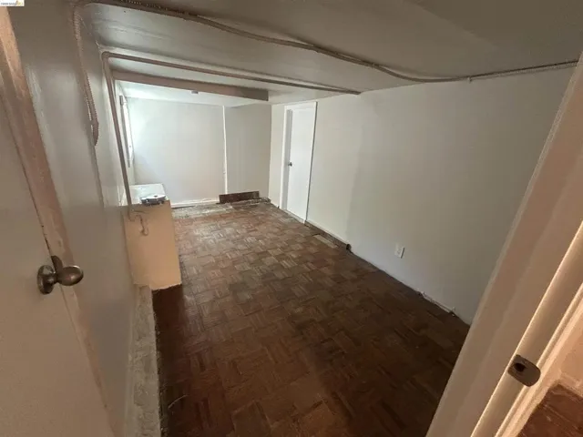 Room featuring wood-finish parquet flooring, white painted walls, and a visible window providing natural light
