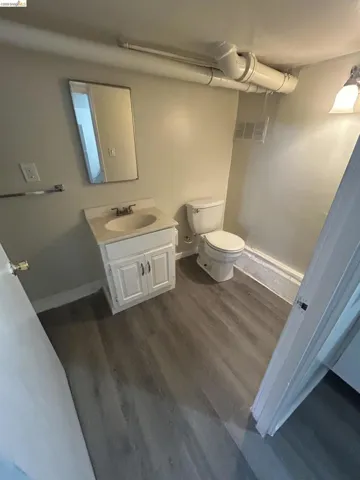 Bathroom featuring wood-finish flooring, a white vanity with a light-colored countertop, and a wall-mounted mirror