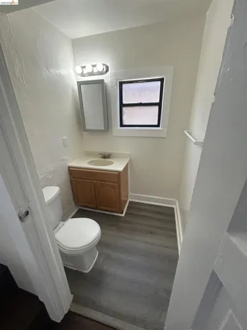 Bathroom featuring wood-finish flooring, a vanity with a light wood finish cabinet, a white countertop, and a white toilet