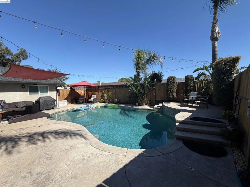 Resort-style backyard featuring a freeform swimming pool with integrated steps, stamped concrete patio, and string lighting