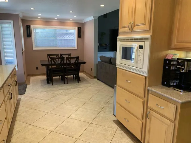 Open-concept kitchen and dining area featuring tile flooring, light wood cabinetry, recessed lighting, and a built-in microwave