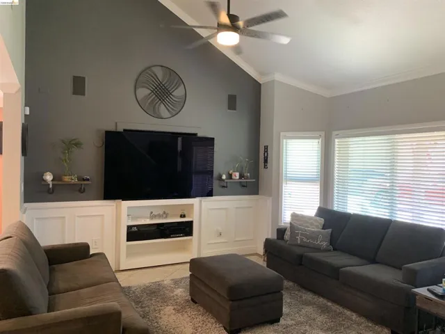 Living space featuring a vaulted ceiling with a ceiling fan, a custom built-in entertainment center, and multiple windows with blinds