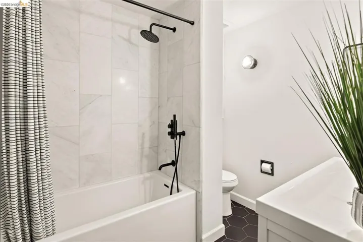 Bathroom featuring a white tub, floor-to-ceiling tiled shower surround, matte black shower fixtures, and dark hexagonal floor tiles