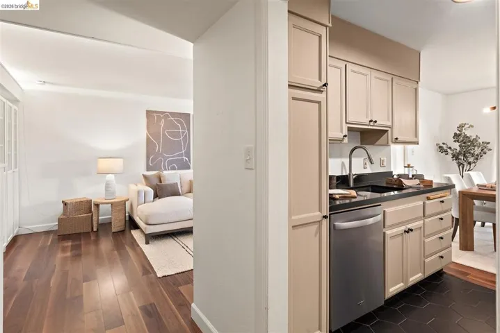 Kitchenette featuring beige cabinetry, dark countertops, a stainless steel dishwasher, and a stainless steel faucet