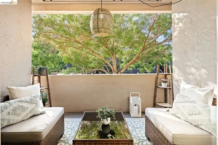 Covered outdoor patio featuring a woven pendant light fixture, textured walls, and a substantial privacy wall