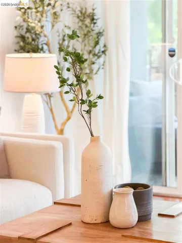 Living area featuring a light-toned sofa, wood coffee table, and a sliding glass door with white curtains providing access to the outdoors