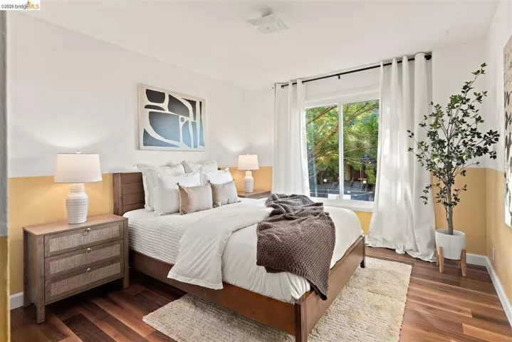 Bedroom featuring wood-finish flooring, a large window, white curtains, and a two-tone painted wall