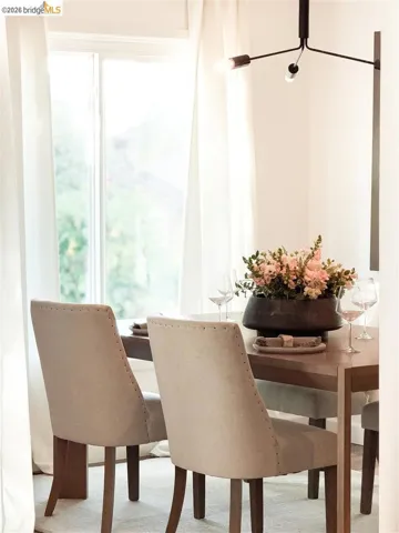 Dining area featuring a contemporary chandelier, large window with sheer white curtains, and wood-finish flooring