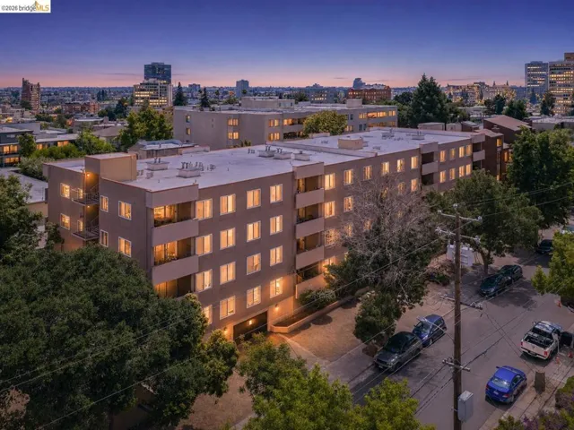 Multi-story residential building featuring a neutral-toned facade, multiple balconies, individual window units, and a flat roofline