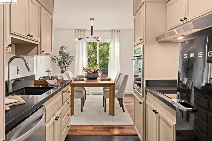 Galley kitchen featuring light-toned cabinetry, dark countertops, a built-in oven, and a modern refrigerator