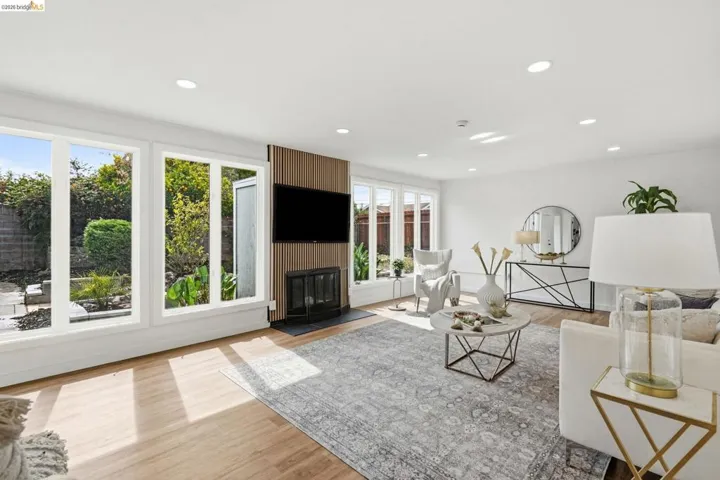 Spacious living area featuring expansive windows, wood-finish flooring, a contemporary fireplace with a slatted wood surround, recessed lighting, and a neutral color palette