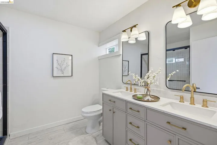 Dual vanity featuring light gray cabinetry, gold-finish hardware, and quartz countertops