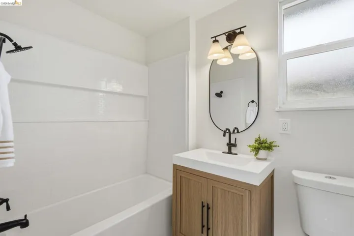 Bathroom featuring a wood-finish vanity with an integrated white sink, matte black faucet, and oval mirror