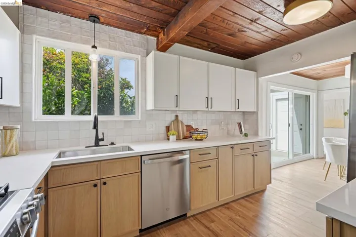 Kitchen featuring a wood-beam ceiling, white shaker-style upper cabinetry, wood-finish lower cabinetry, white countertops, and a stainless steel dishwasher