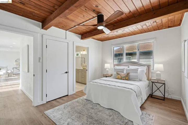 Room featuring a wood-finish plank ceiling with exposed beams, overhead ceiling fan with light, three-pane window, and light wood-finish flooring