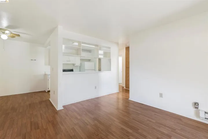 Open-concept living area featuring wood-finish flooring, white walls, and a ceiling fan with integrated lighting