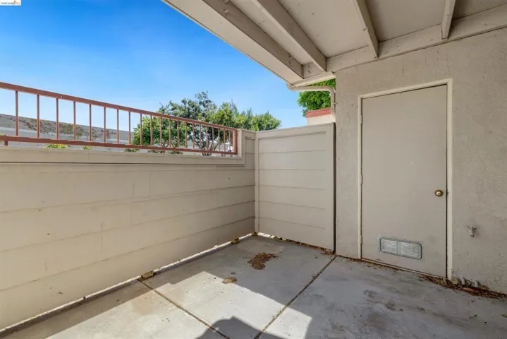 Covered concrete patio space featuring a stucco exterior wall, a utility door, and an exterior light fixture