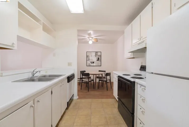 Galley kitchen featuring white cabinetry, white countertops, a double basin stainless steel sink, and a black electric range