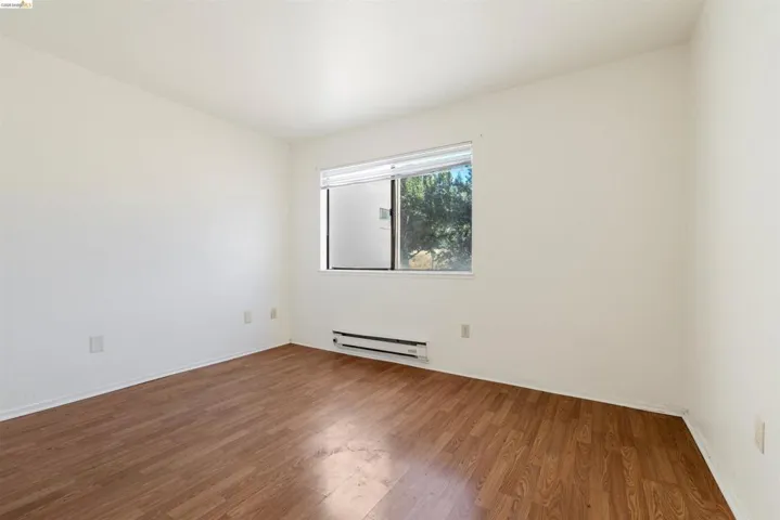 Room featuring wood-finish flooring, white walls, and a window with horizontal blinds