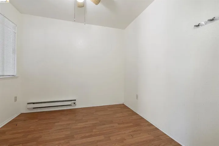 Room featuring wood-finish flooring, white walls, and a window with blinds