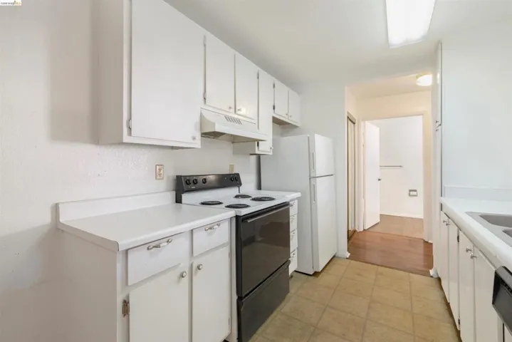 Kitchen featuring white cabinetry, white countertops, a black range with an overhead vent, and a white refrigerator