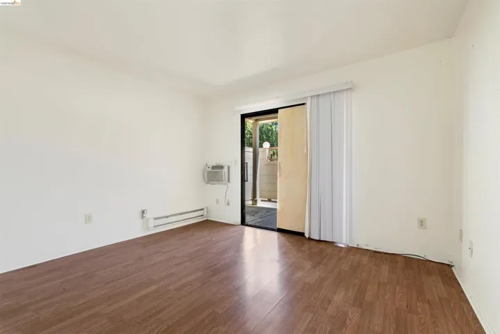 Open-concept room featuring wood-finish flooring, white walls, a sliding glass door, an in-wall air conditioning unit, and baseboard heating