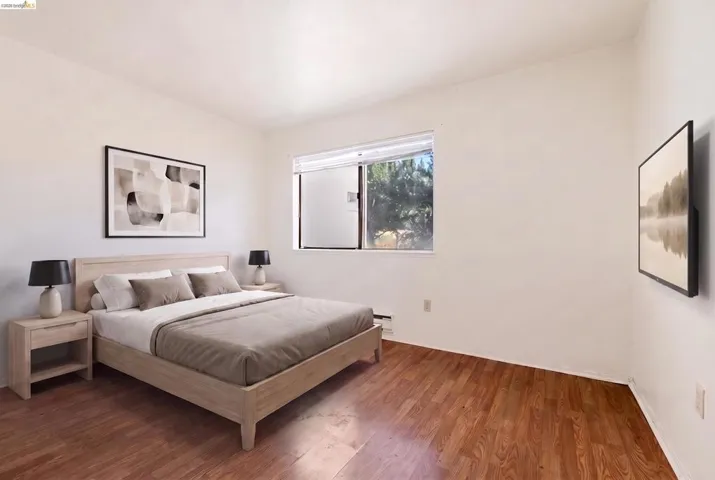 Bright interior space featuring wood-finish flooring, a large window, white walls, and baseboard heating