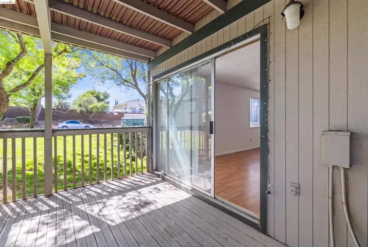 Covered wood-plank patio with a wood railing, offering outdoor access through a glass sliding door