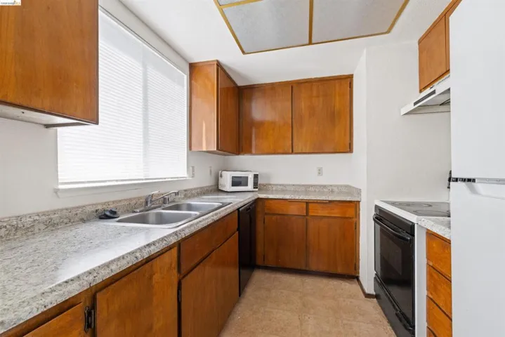 Kitchen featuring wood cabinetry, light-toned countertops, a double basin stainless steel sink, and a white refrigerator