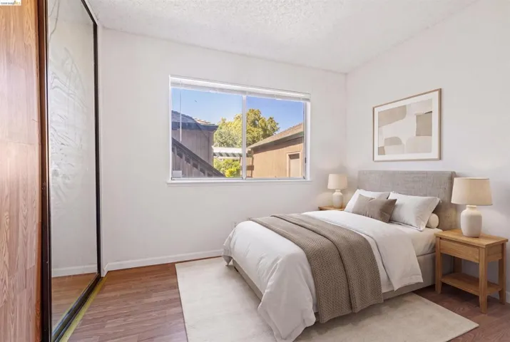 Bedroom featuring wood-finish flooring, a large window, and mirrored sliding closet doors