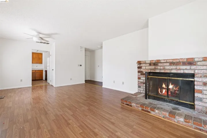 Living space featuring a brick fireplace with a glass enclosure, wood-finish flooring, and a ceiling fan
