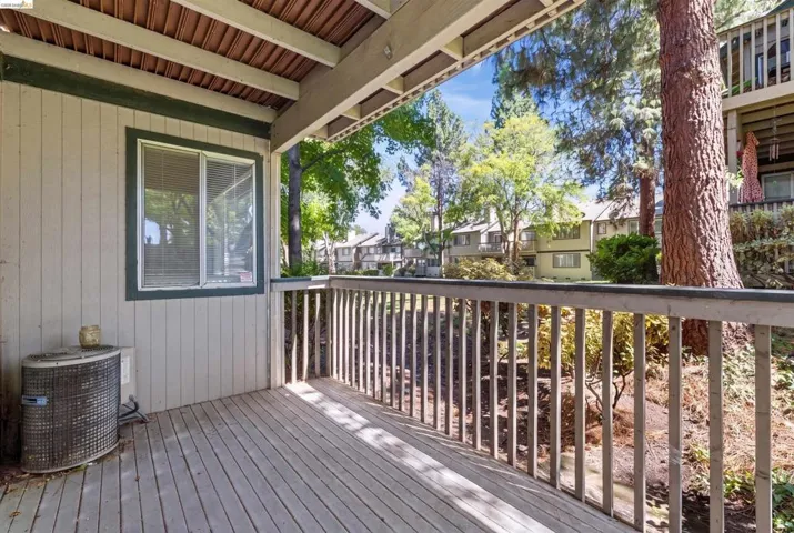Outdoor deck featuring natural wood-finish flooring, a wood-slat railing, and a window with blinds