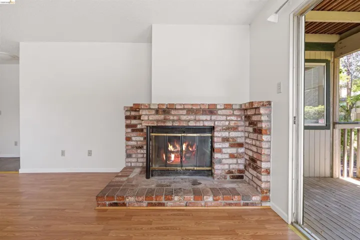 Brick fireplace with a hearth, wood-finish flooring, white walls, and a sliding glass door leading to an outdoor deck