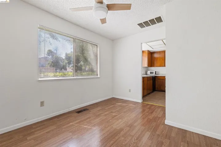 Room featuring wood-finish flooring, a large window with horizontal blinds, and a ceiling fan with integrated lighting