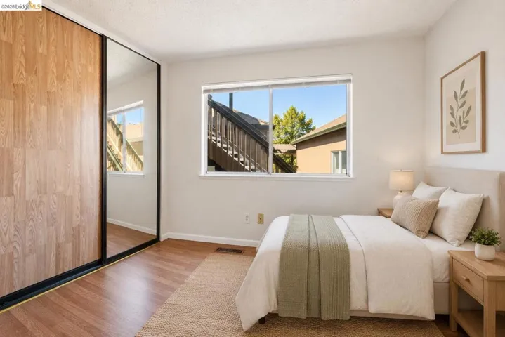 Room featuring wood-finish flooring, a window with exterior views, and a full-wall closet with wood-finish and mirrored sliding doors